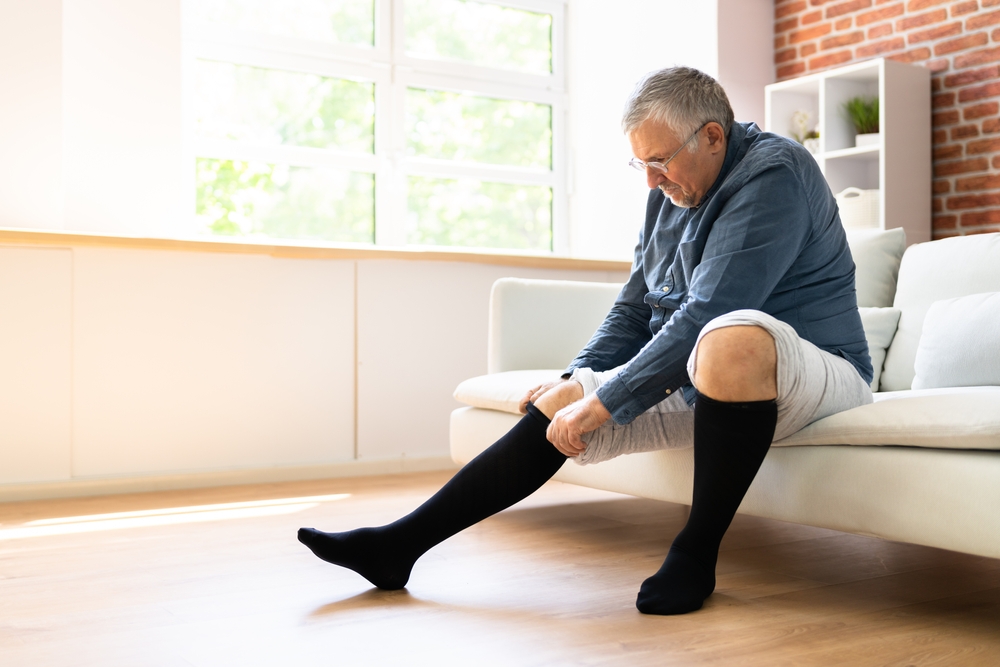 Older,Male,Sitting,On,Couch,Putting,On,Compression,Stockings,Compression,Socks,Leg,Ulcer,Varicose,Veins.