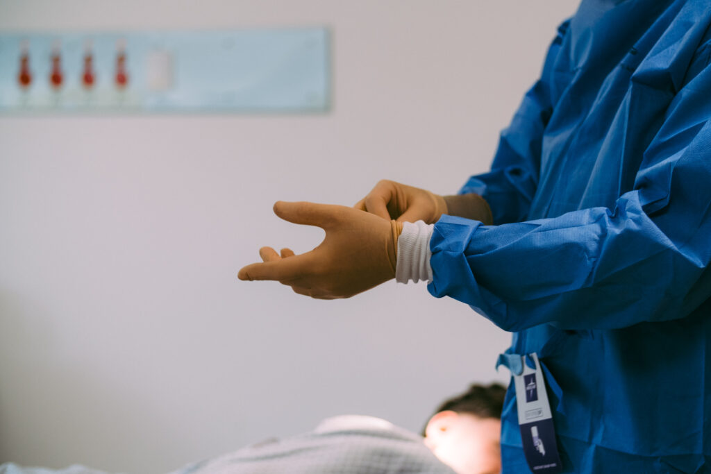 Surgeon,Prepares,For,Varicose,Vein,Treatment,Wearing,Sterile,Scrubs,And,Gloves,Patient,In,Background,Lying,On.Bed.
